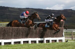 Two horses jump a fence at Cheltenham racecourse.